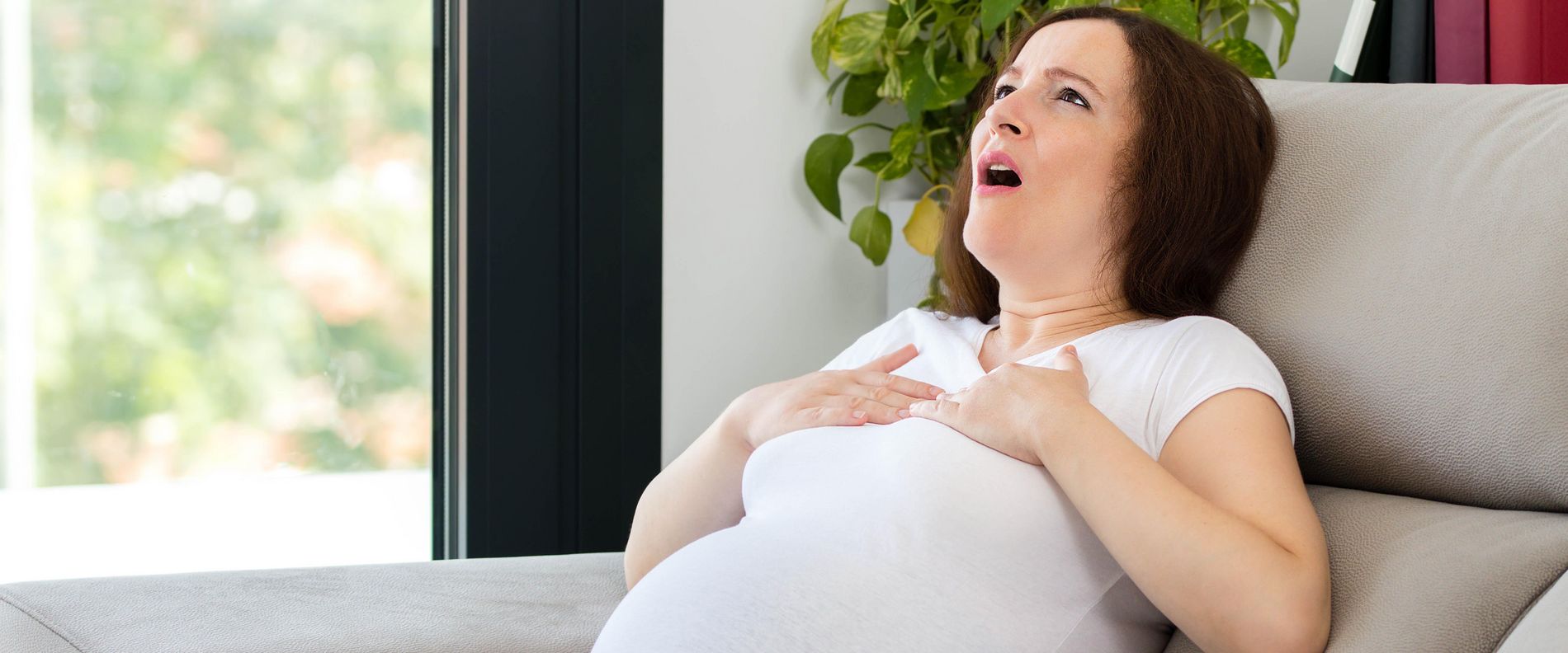 Eine schwangere Frau sitzt auf dem Sofa und hat Atemnot