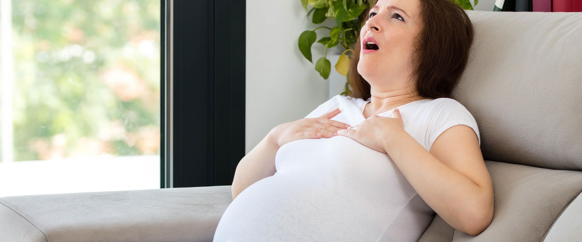 Eine schwangere Frau sitzt auf dem Sofa und hat Atemnot